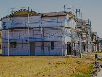 Newly constructed residential homes with exterior scaffolding installed for siding or finishing work in a developing suburban neighborhood.
