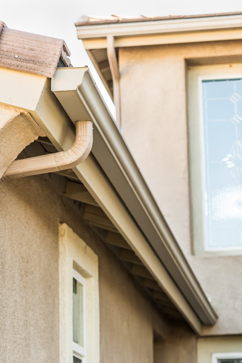 residential-seamless-gutter-installation Close-up view of seamless gutters and downspouts installed along the roofline of a modern residential home exterior.