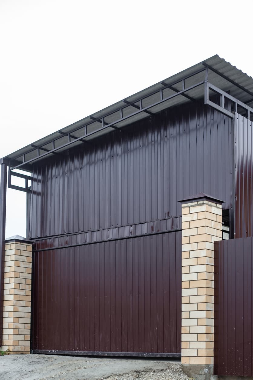 Modern residential home featuring dark vertical metal siding with brick columns. The image highlights durable, low-maintenance metal cladding with a clean, contemporary exterior design.
